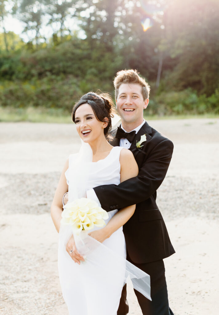 Portrait of bride and Groom on  Rosewood Beach in Highland Park standing on the sand laughing at the camera