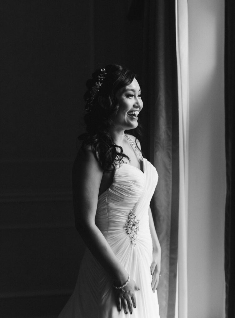 Bridal portrait of bride smiling looking out the window as window light falls on her