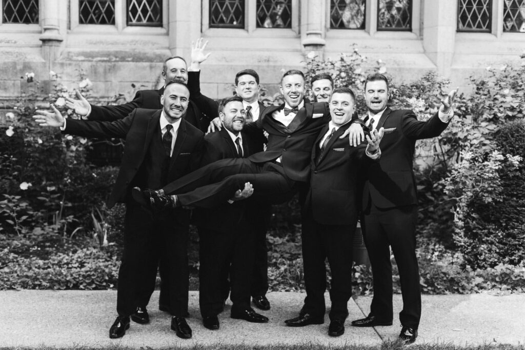 Groomsmen laughing as they lift up and hold groom
