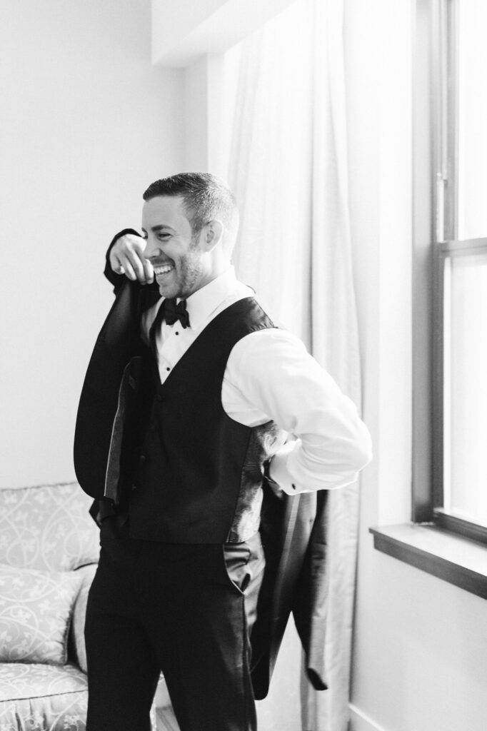 Groom smiling as he candidly puts on his jacket