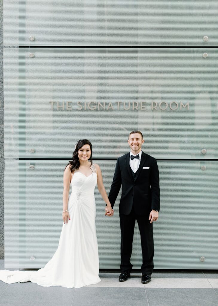 Bride and groom smiling in front of the Signature Room at the 95th sign