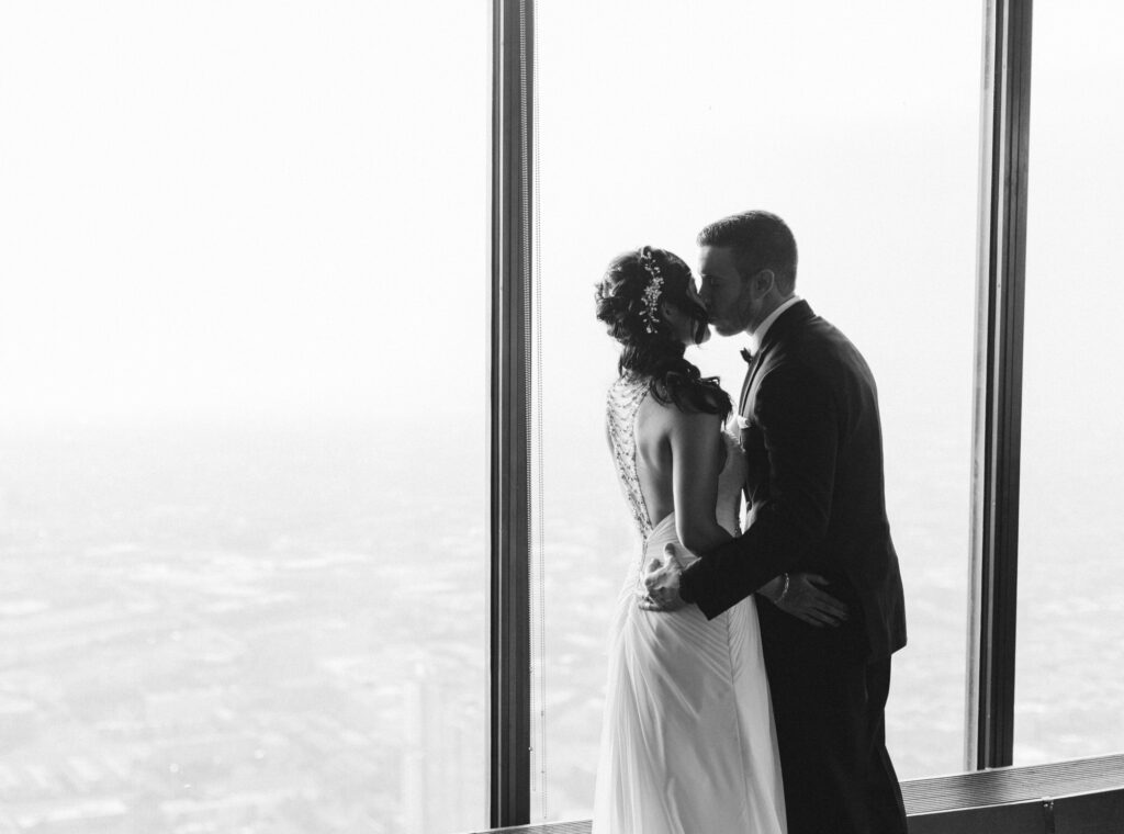 Chicago city views outside a large window as the Bride and Groom kiss at the Signature Room at the 95th