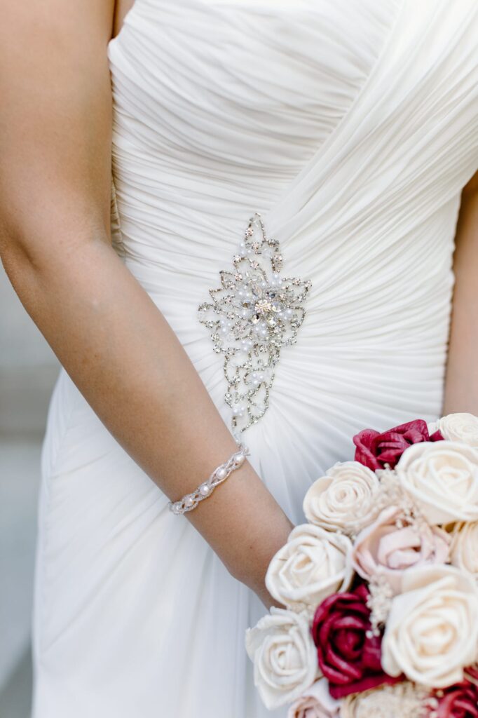 Close up details of the Brides dress while she holds her bouquet