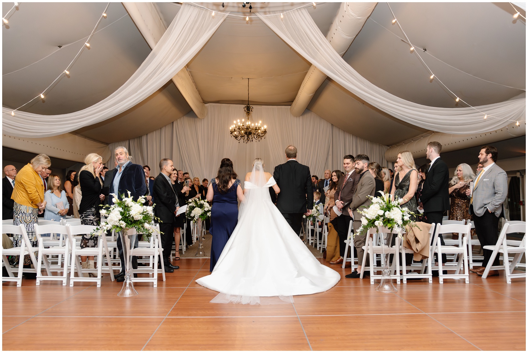 A bride is walked down the aisle as guests stand to watch