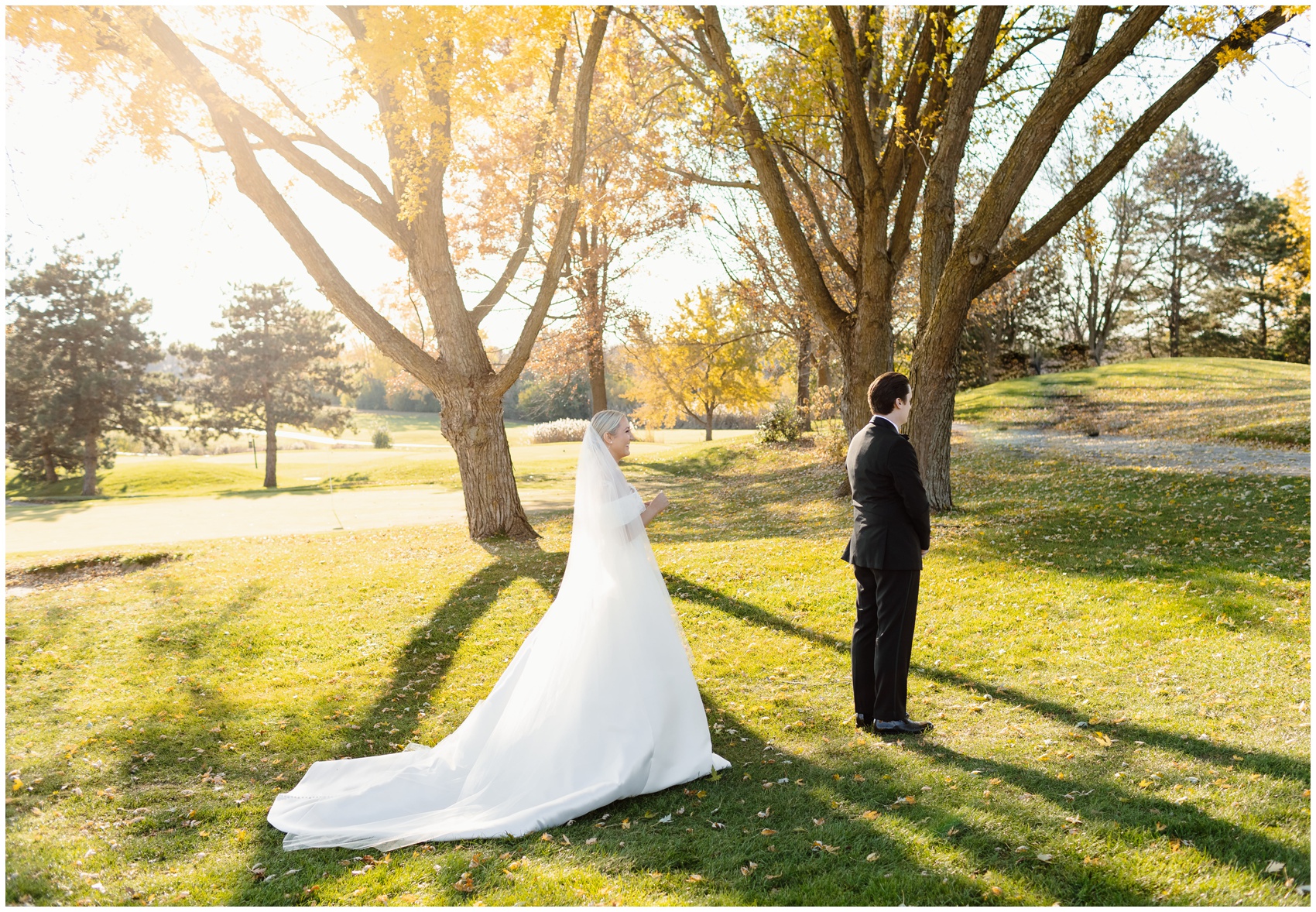 Newlyweds wait for their first look in a park lawn at sunset