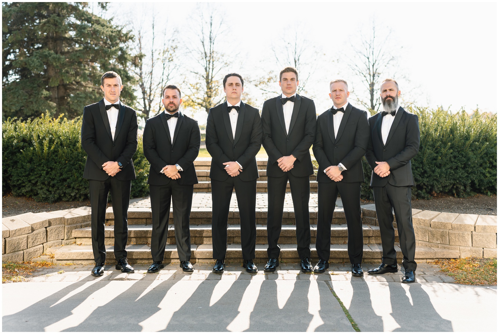 A groom stands by a patio staircase with hands crossed in front of him with his groomsmen