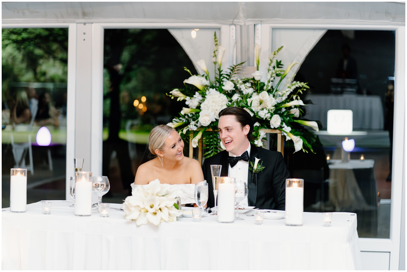 A bride and groom laugh while sitting at their head table in their Hyatt Lodge Oak Brook Wedding reception