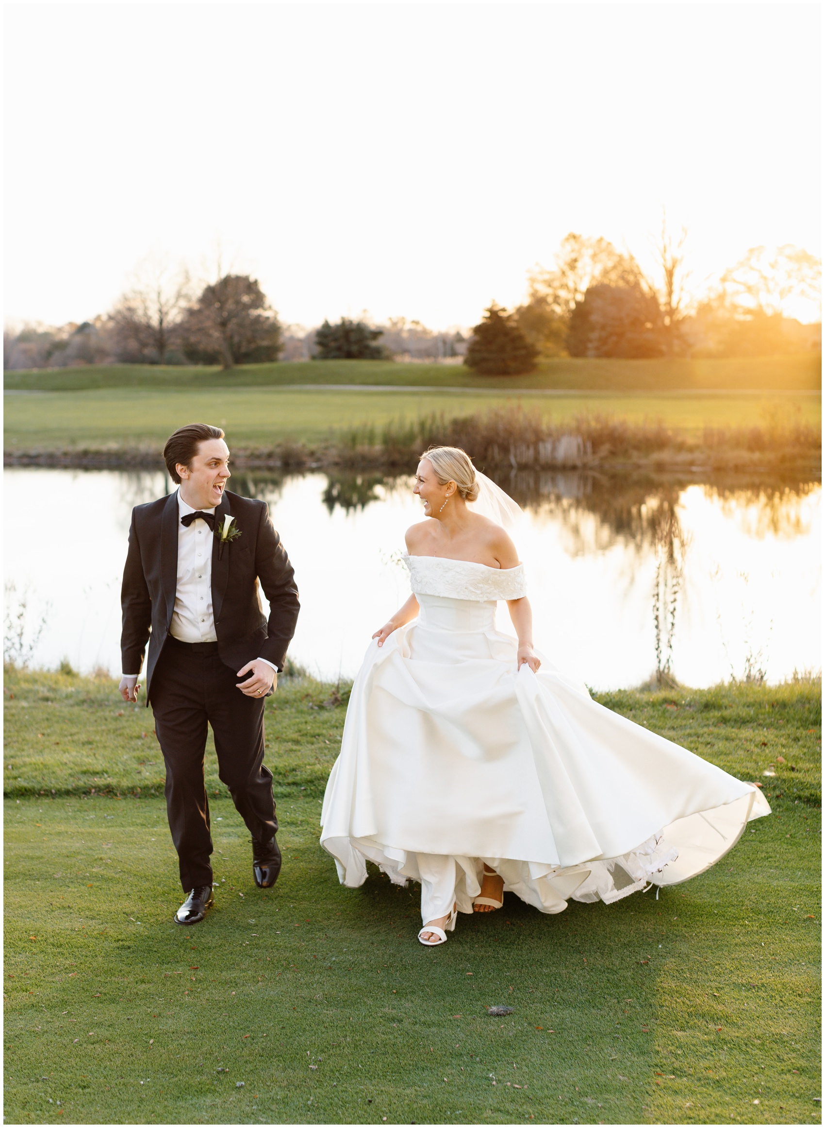 A bride and groom laugh while walking up a golf green by a lake at their Hyatt Lodge Oak Brook Wedding