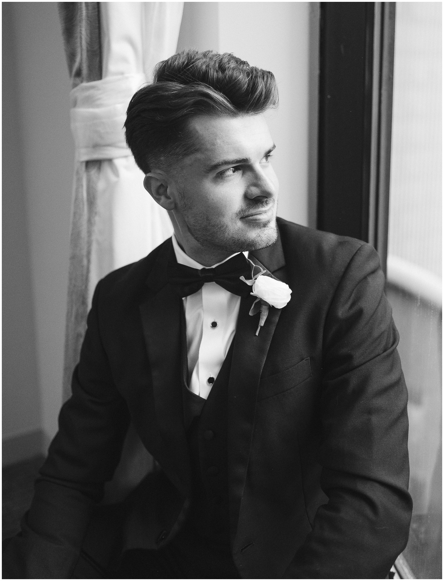 A groom looks over his shoulder out a window while in his getting ready room