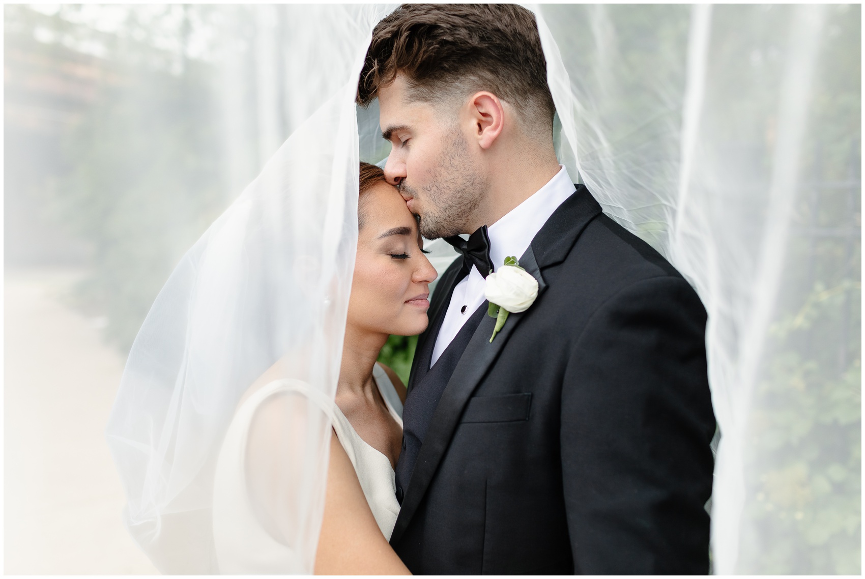 Newlyweds share an intimate moment under the large veil in a garden