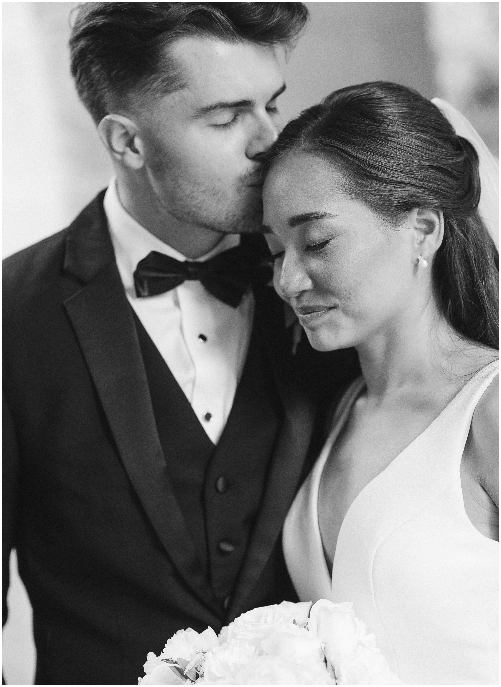 A groom kisses the head of his smiling bride as she leans into him