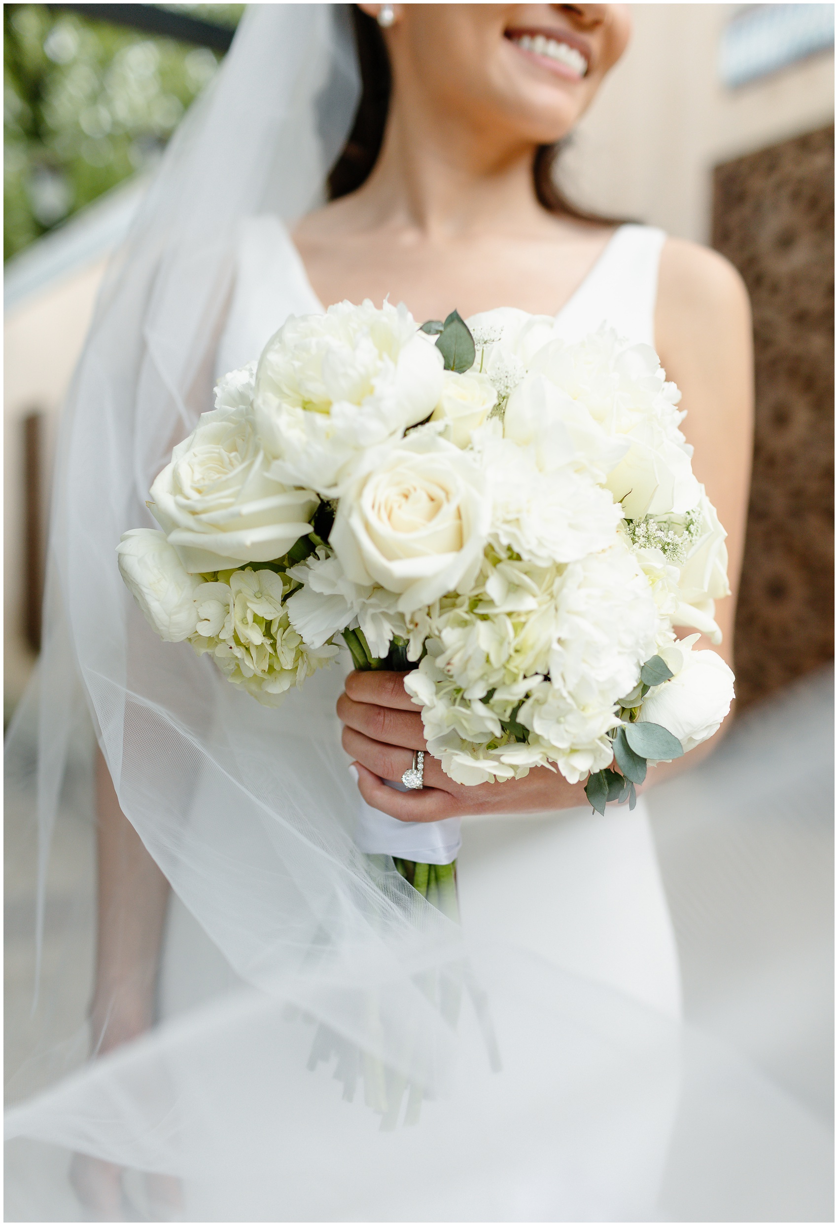 Details of a bride's white rose bouquet while she smiles and holds it