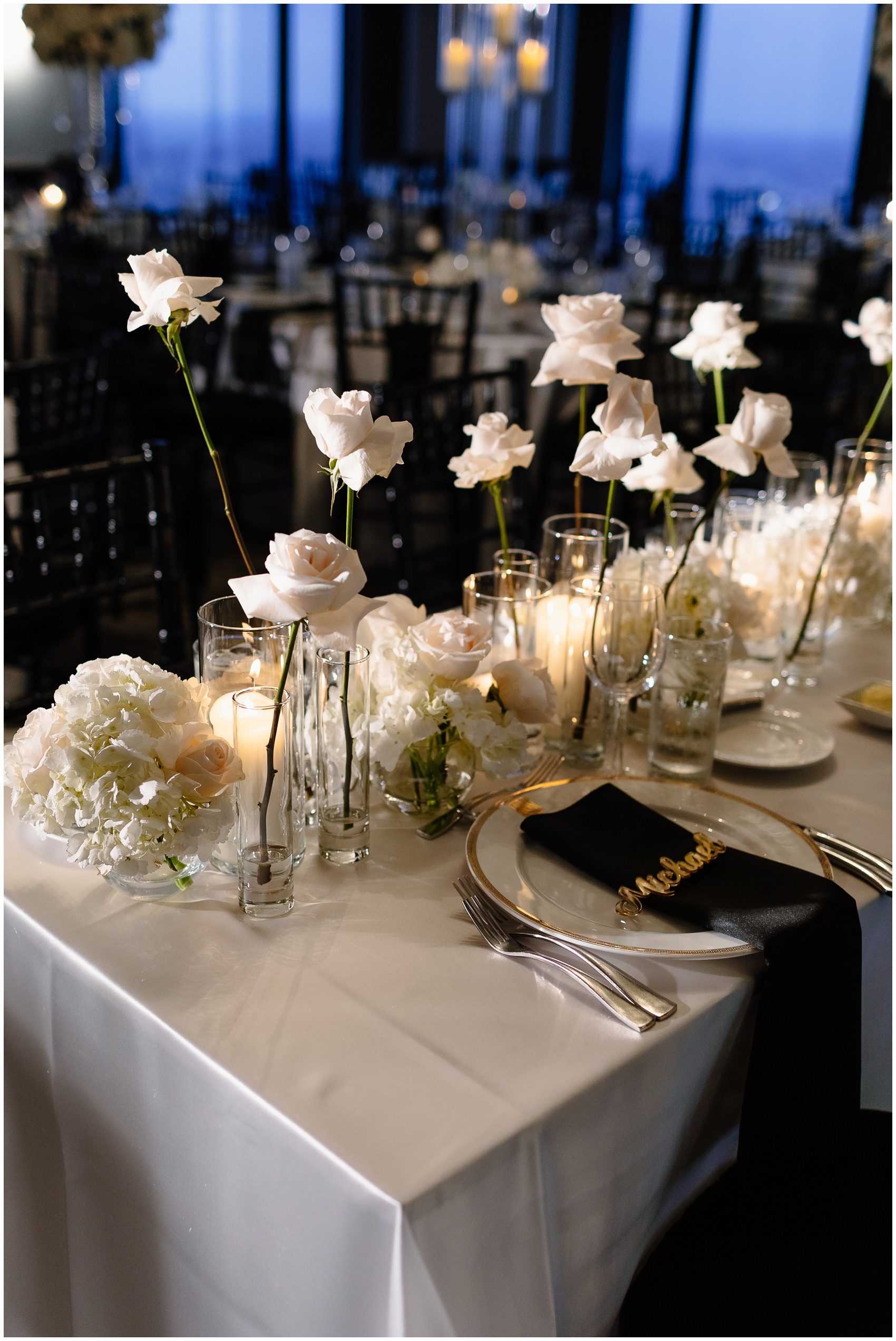 Details of a head table with white roses, candles and custom name covers on black linen set up by Chicago Wedding Planners