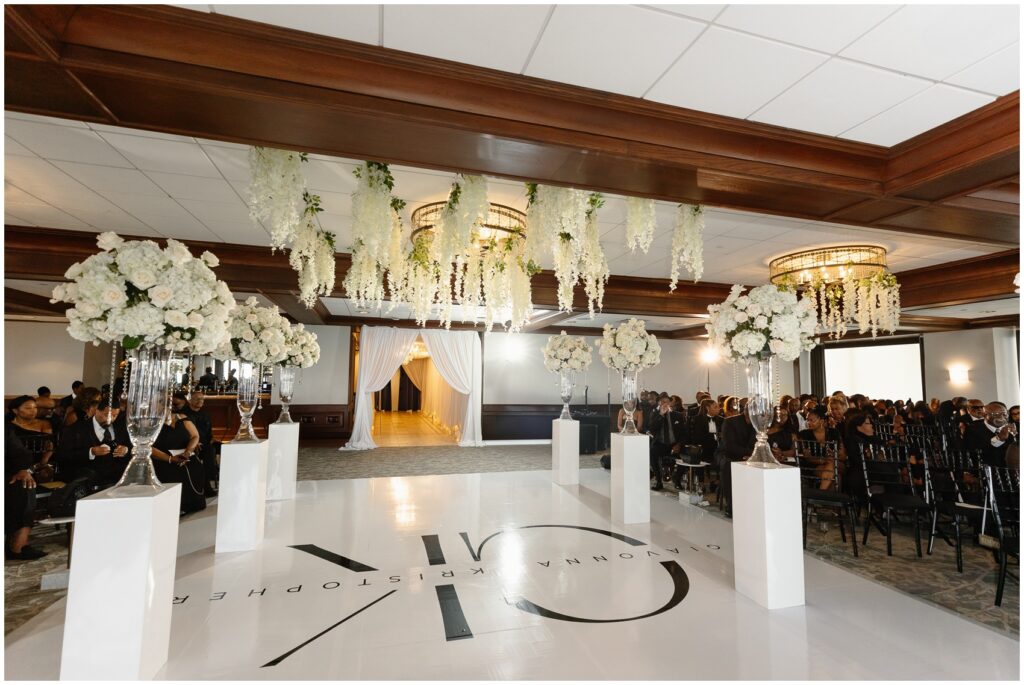 Details of a wedding reception dance floor with hanging white flowers on the chandeliers with guests at tables