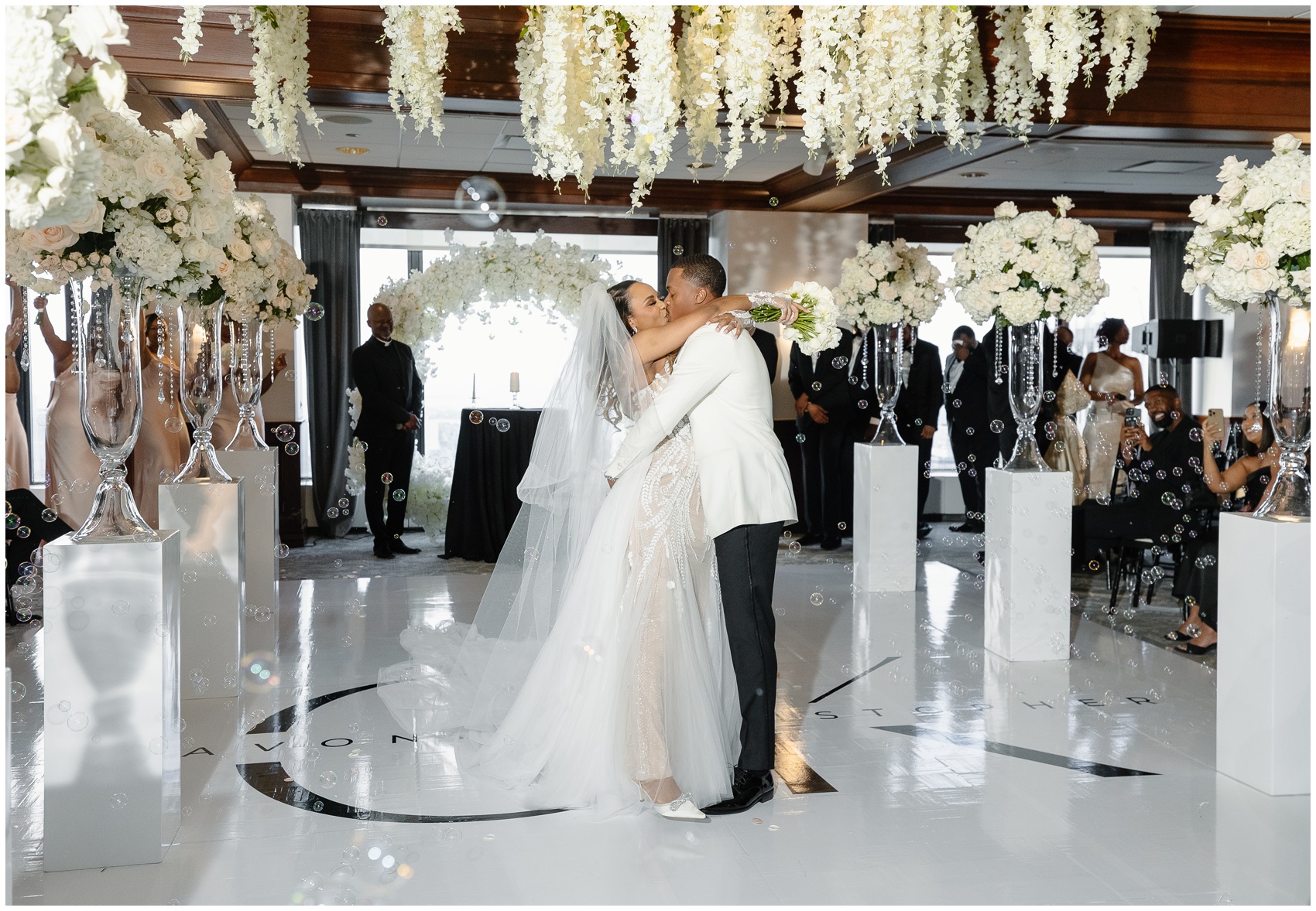 Newlyweds kiss under hanging flowers on the dance floor lined with white roses on pedestals designed by Chicago Wedding Planners