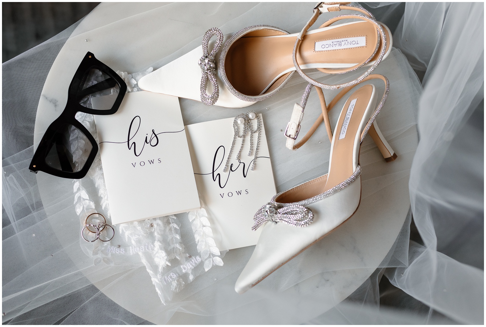 Details of a bride's shoes, sunglasses and jewelry on a marble table