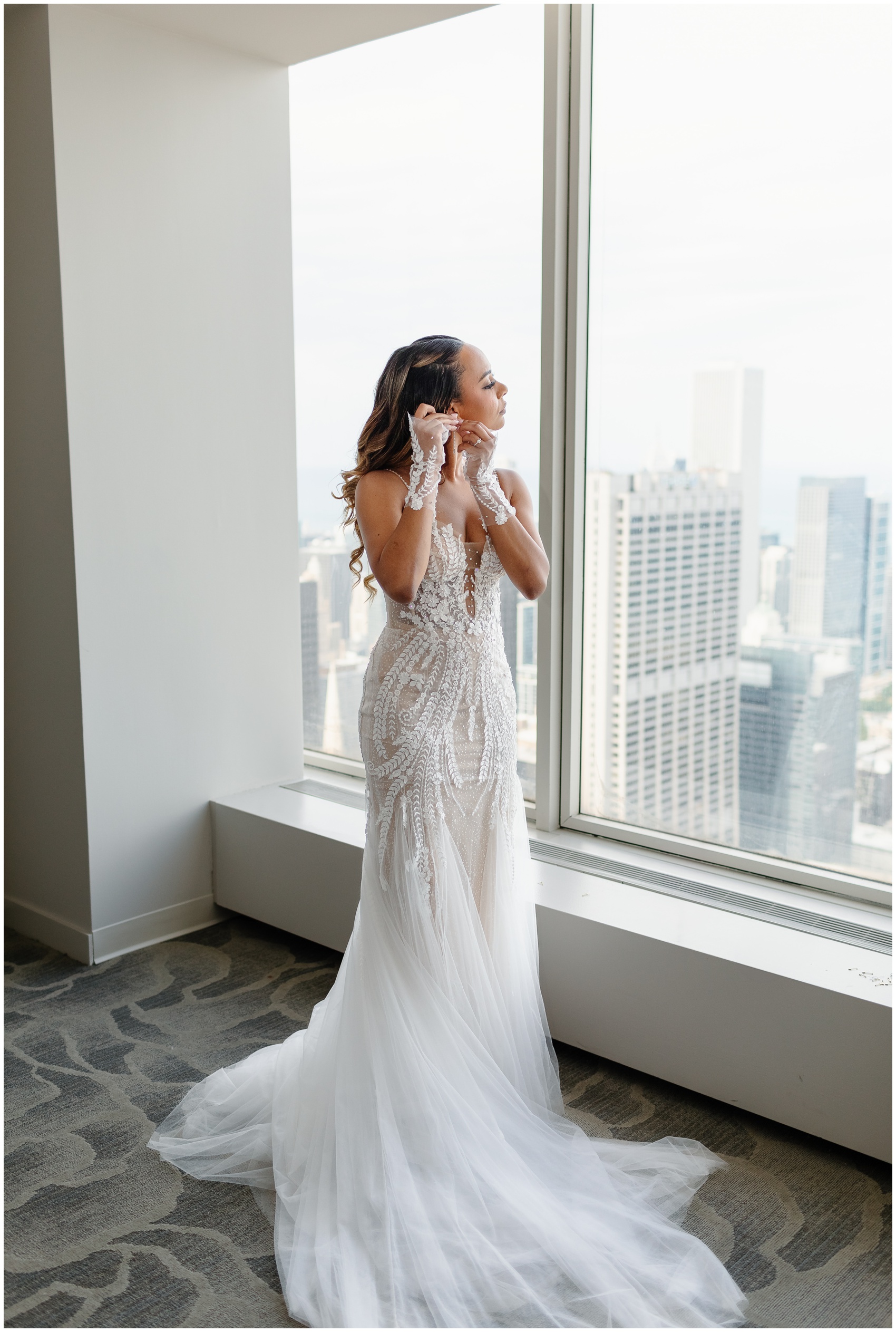 A bride puts on her earrings in a large hotel window