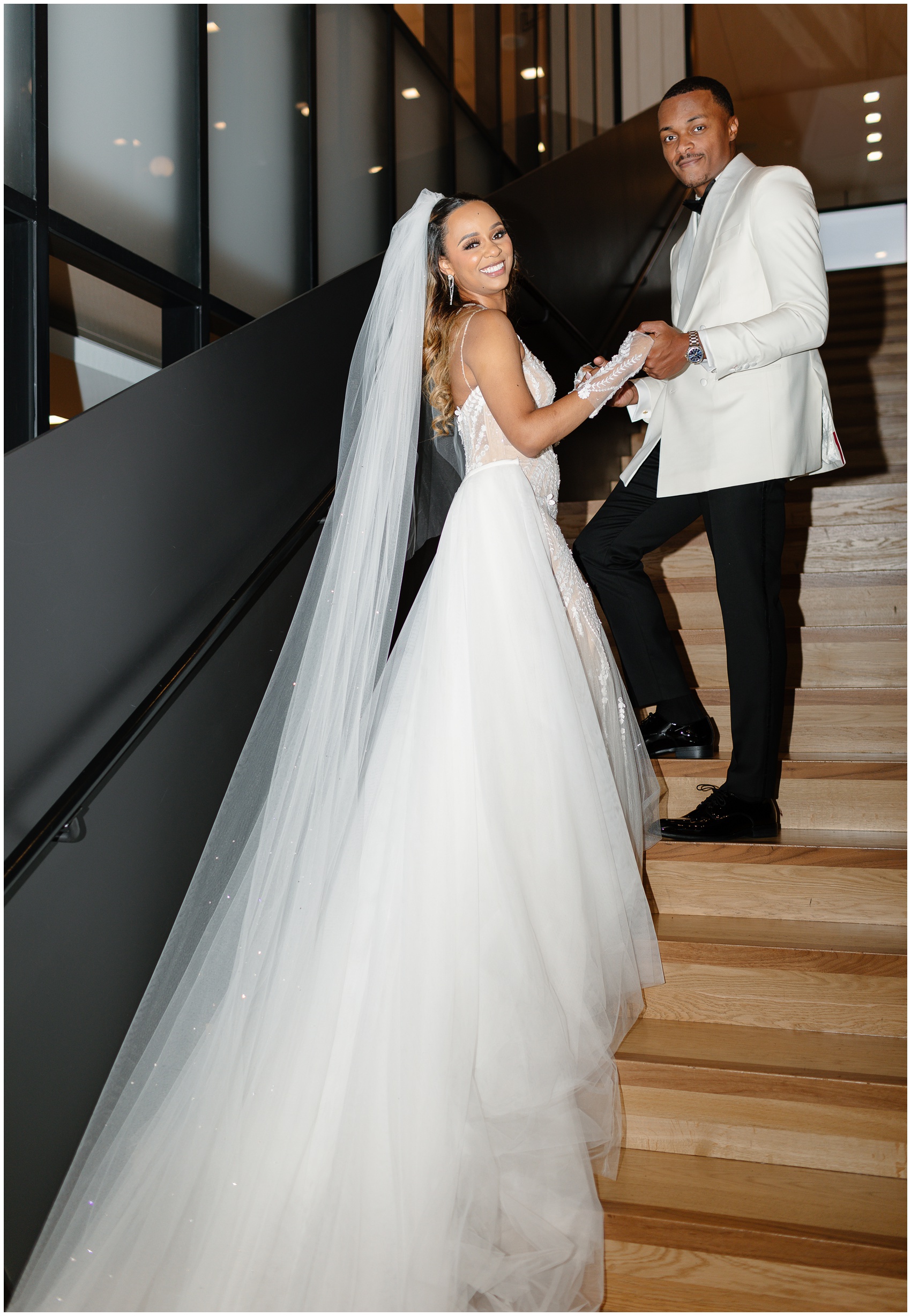 Newlyweds walk up a large wooden staircase at their venue while holding hands