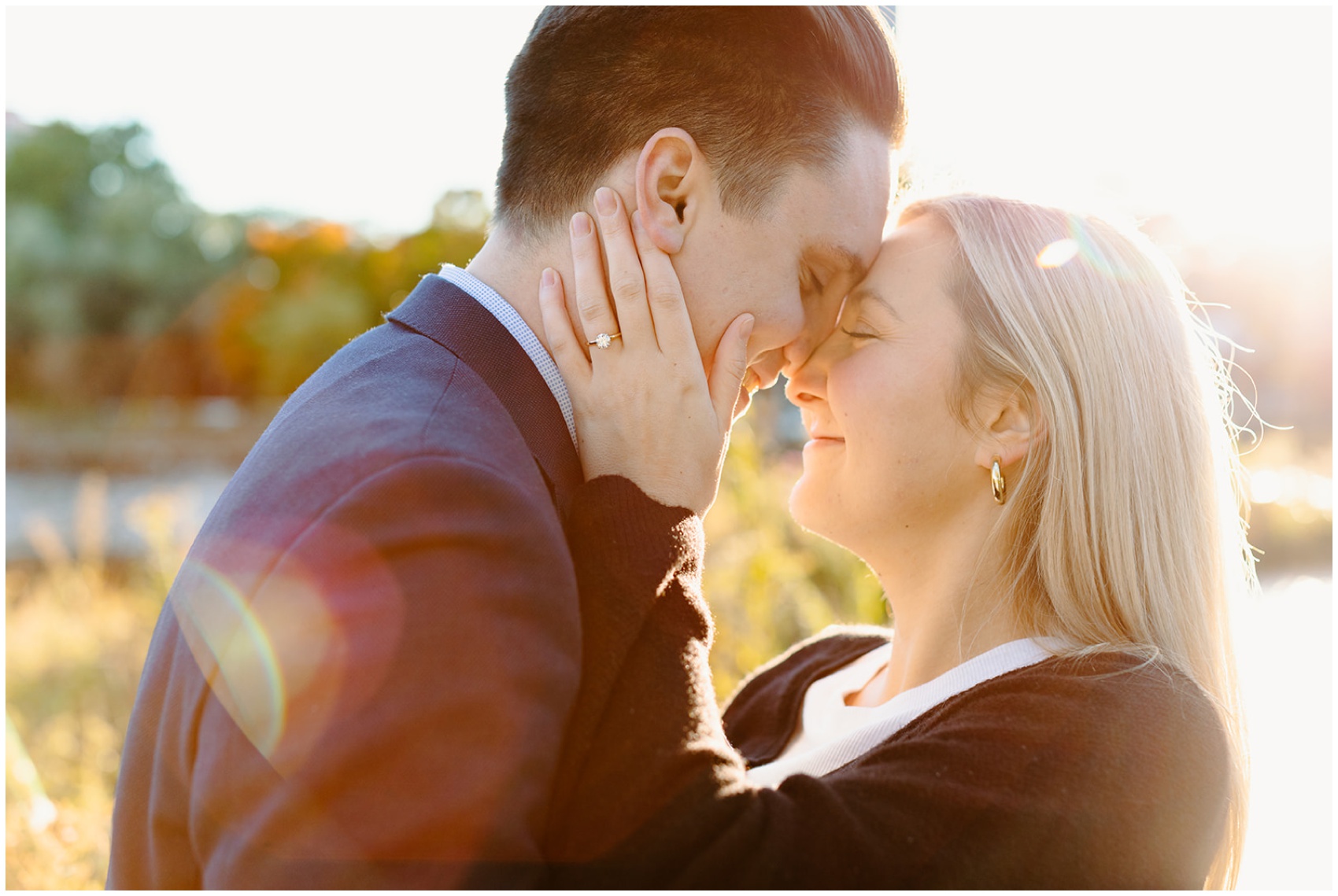 A happy couple snuggles touching foreheads after becoming engaged on a dock at sunset