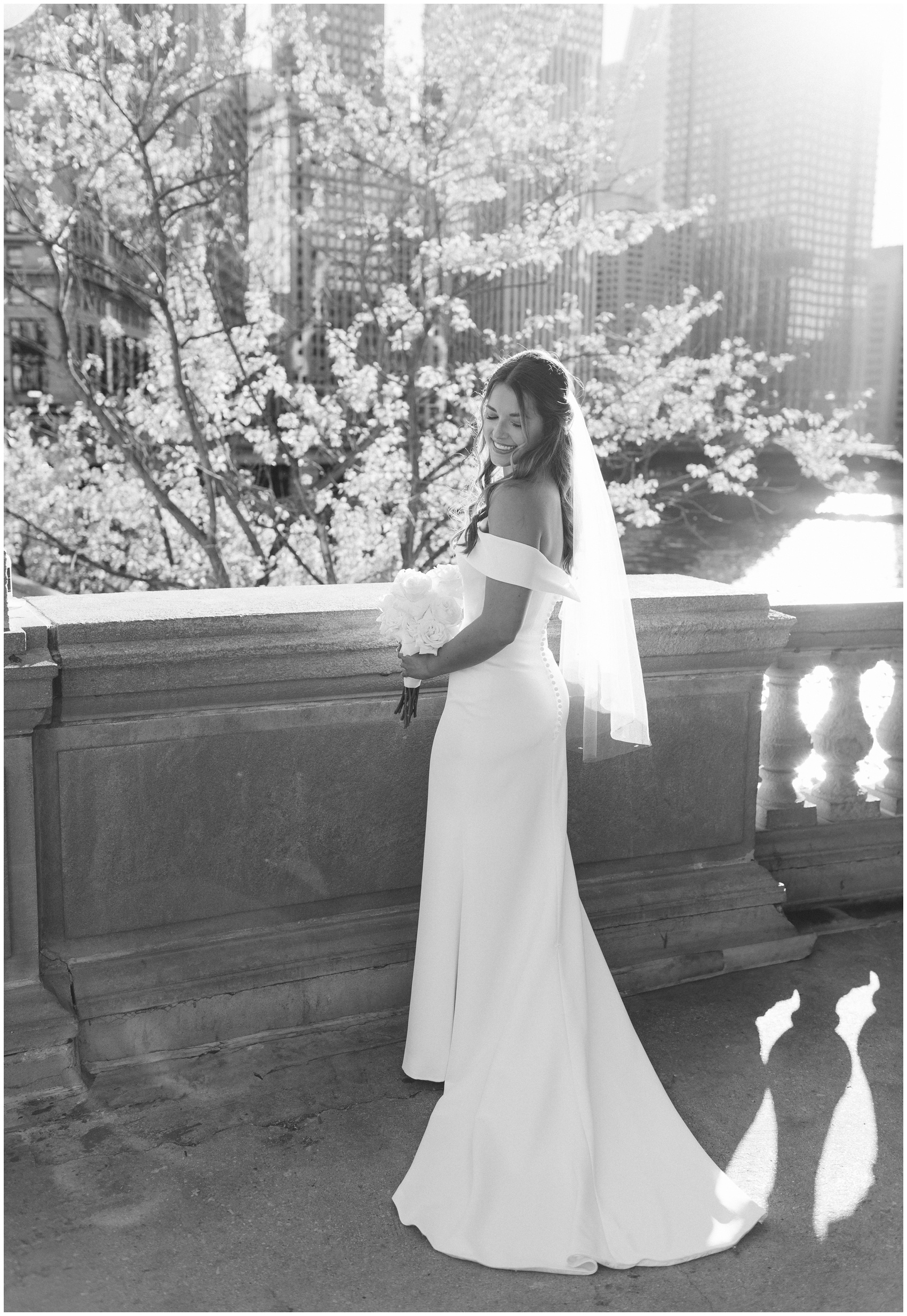 A bride smiles down her shoulder while standing on a bridge over the river after her city hall wedding in chicago