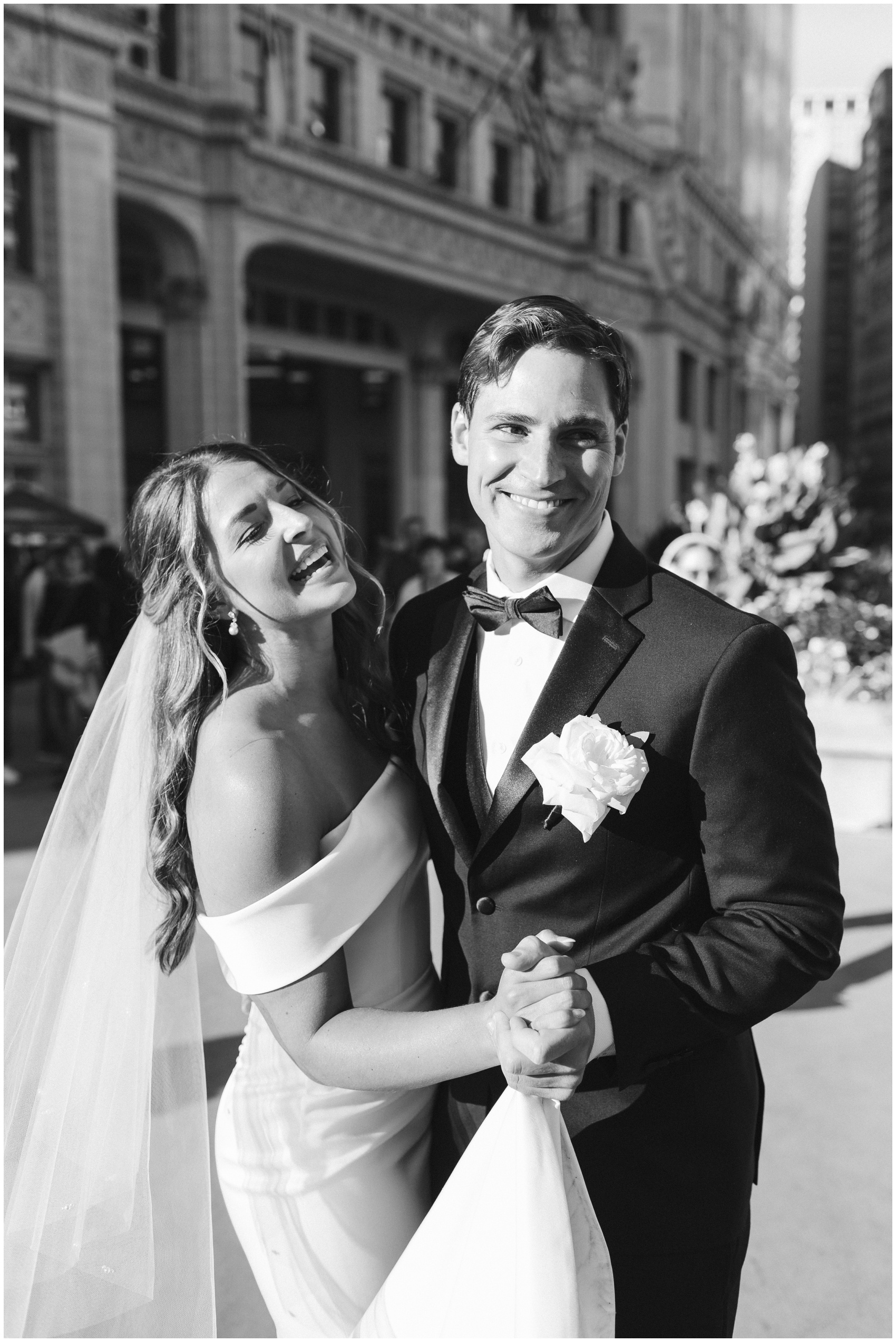 A happy newlywed couple dances in the street in the sun while laughing