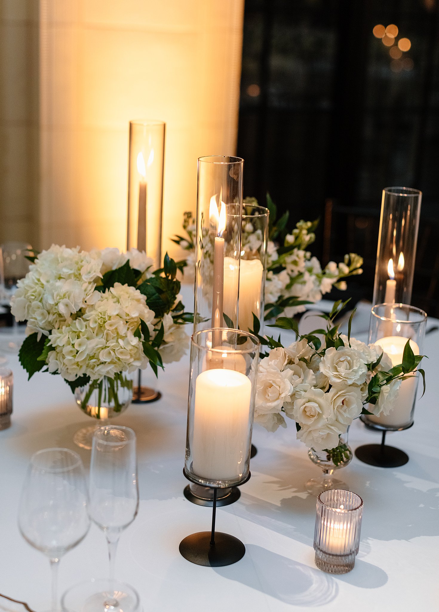 Candles and roses sit on a table of a wedding reception with matching white linen