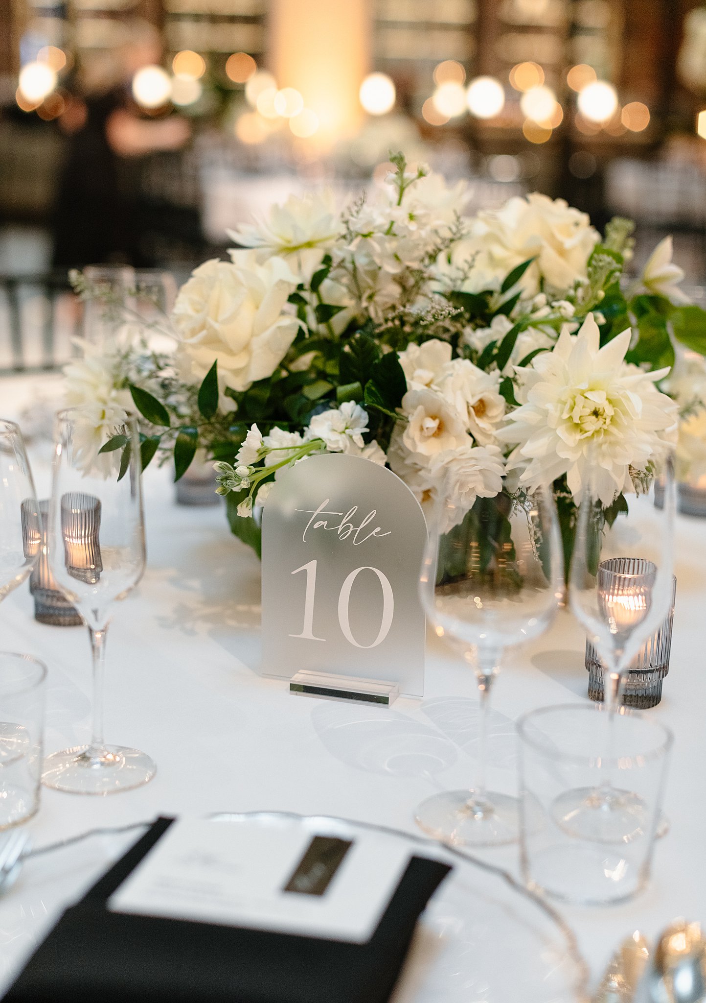 Details of a table sign on white linen with a white floral bouquet centerpiece