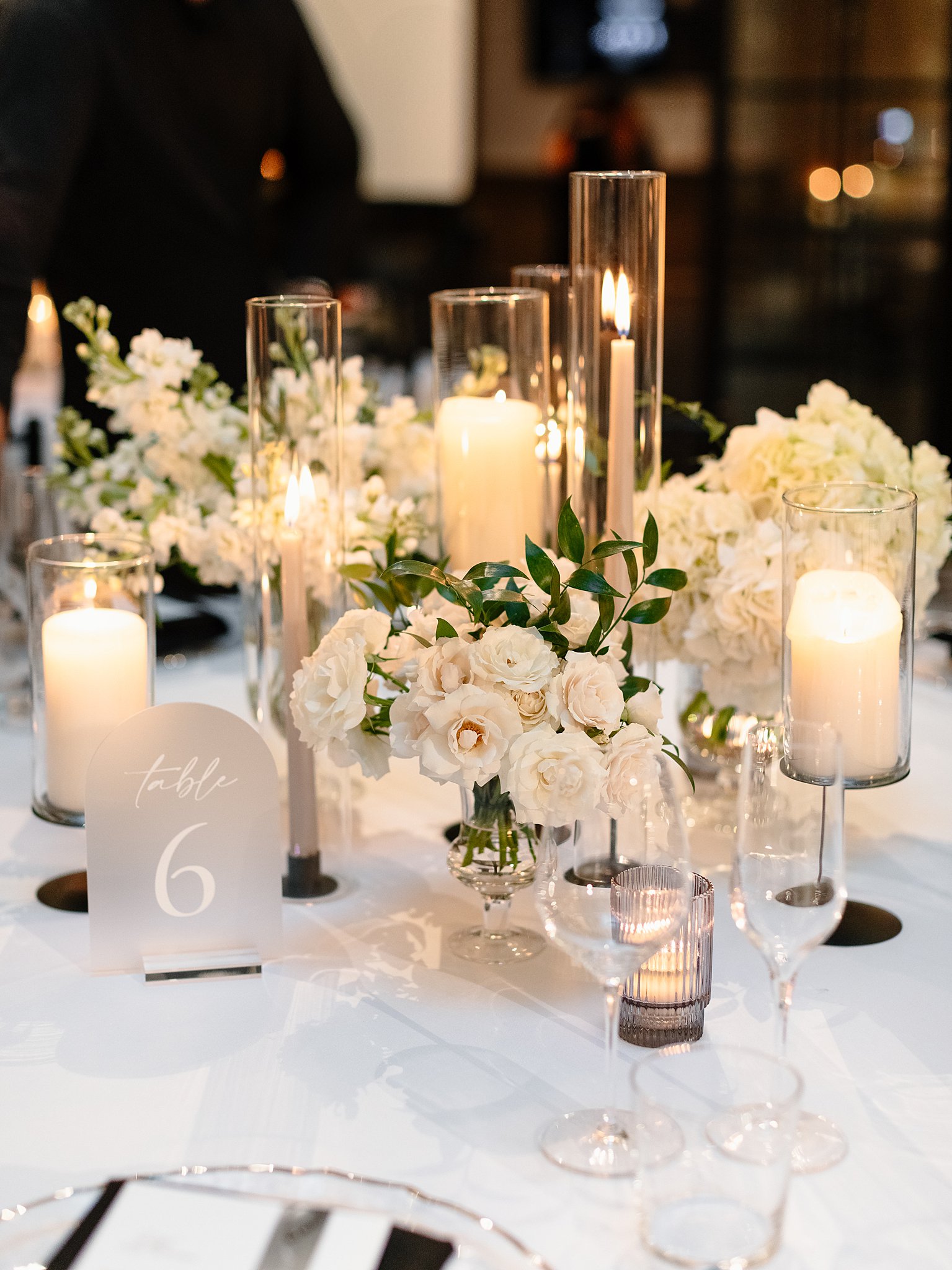 A look at a wedding reception table with white roses, linen and clear glasses and tall candles