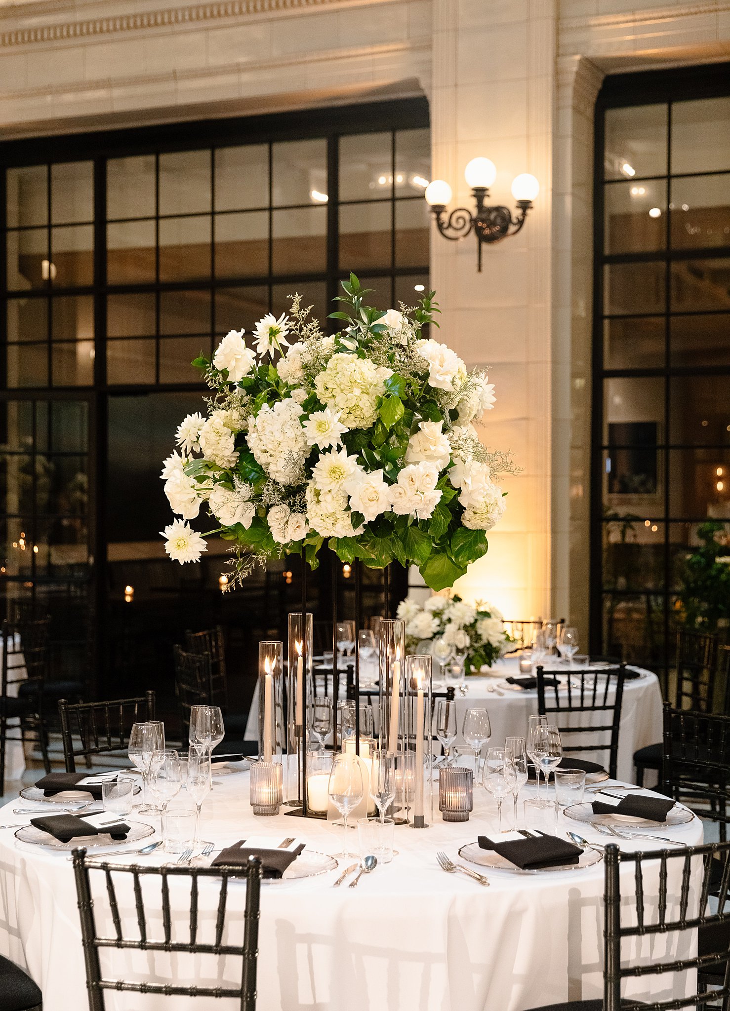 A Downtown Chicago Wedding Venues round reception table with black chairs and napkins on white linen with tall white floral centerpiece