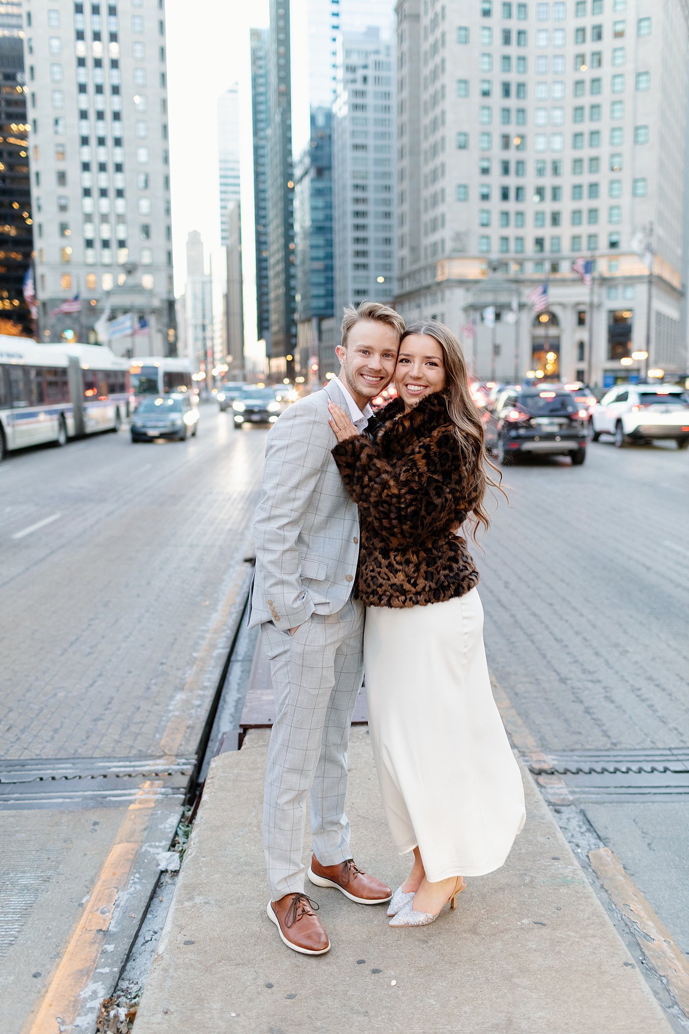 Winter engagement photos in chicago of a happy couple cuddling in the middle of the street in a grey suit and fur jacket