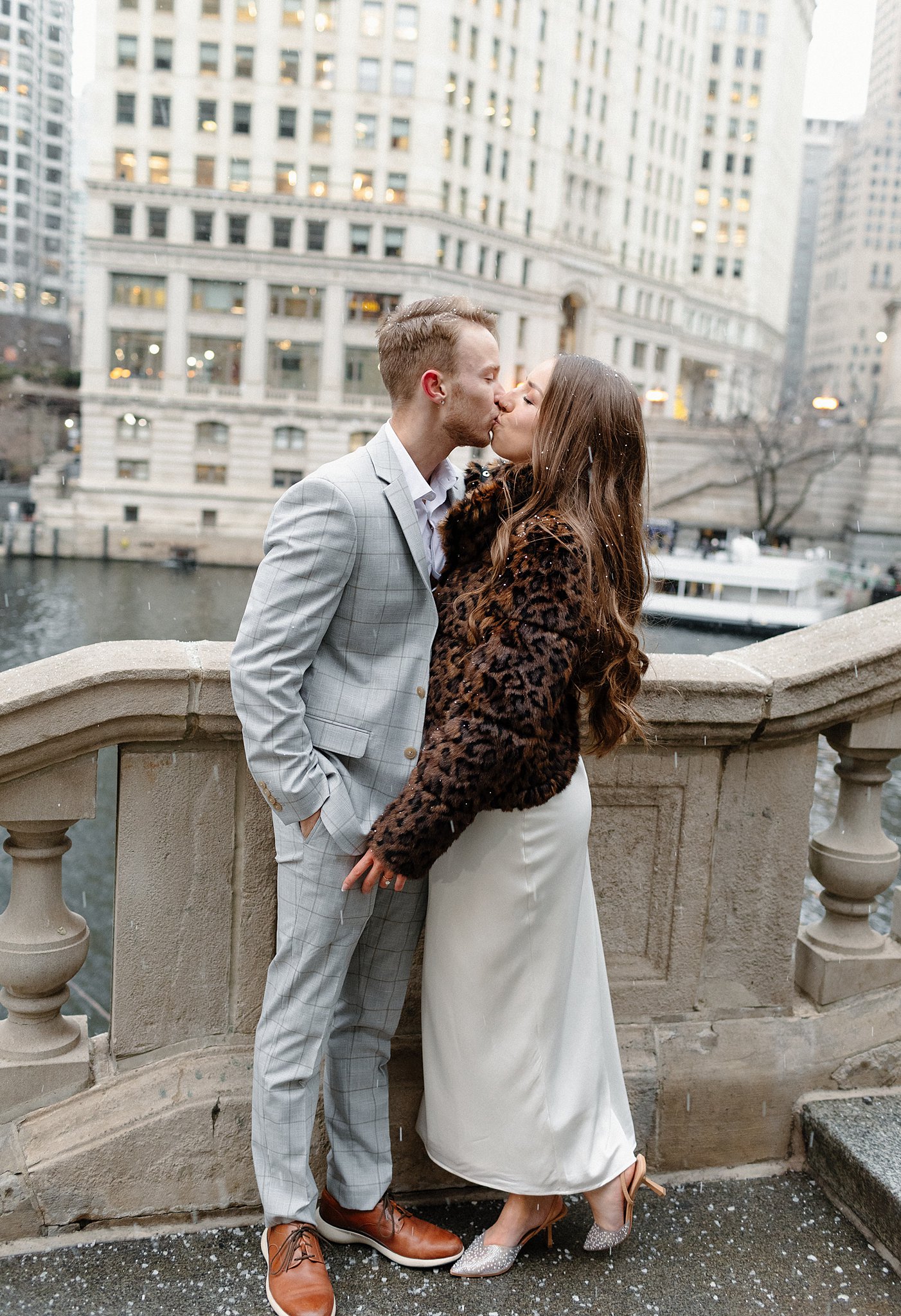 A newly engaged couple kisses on a bridge while it snows during their winter engagement photos in chicago