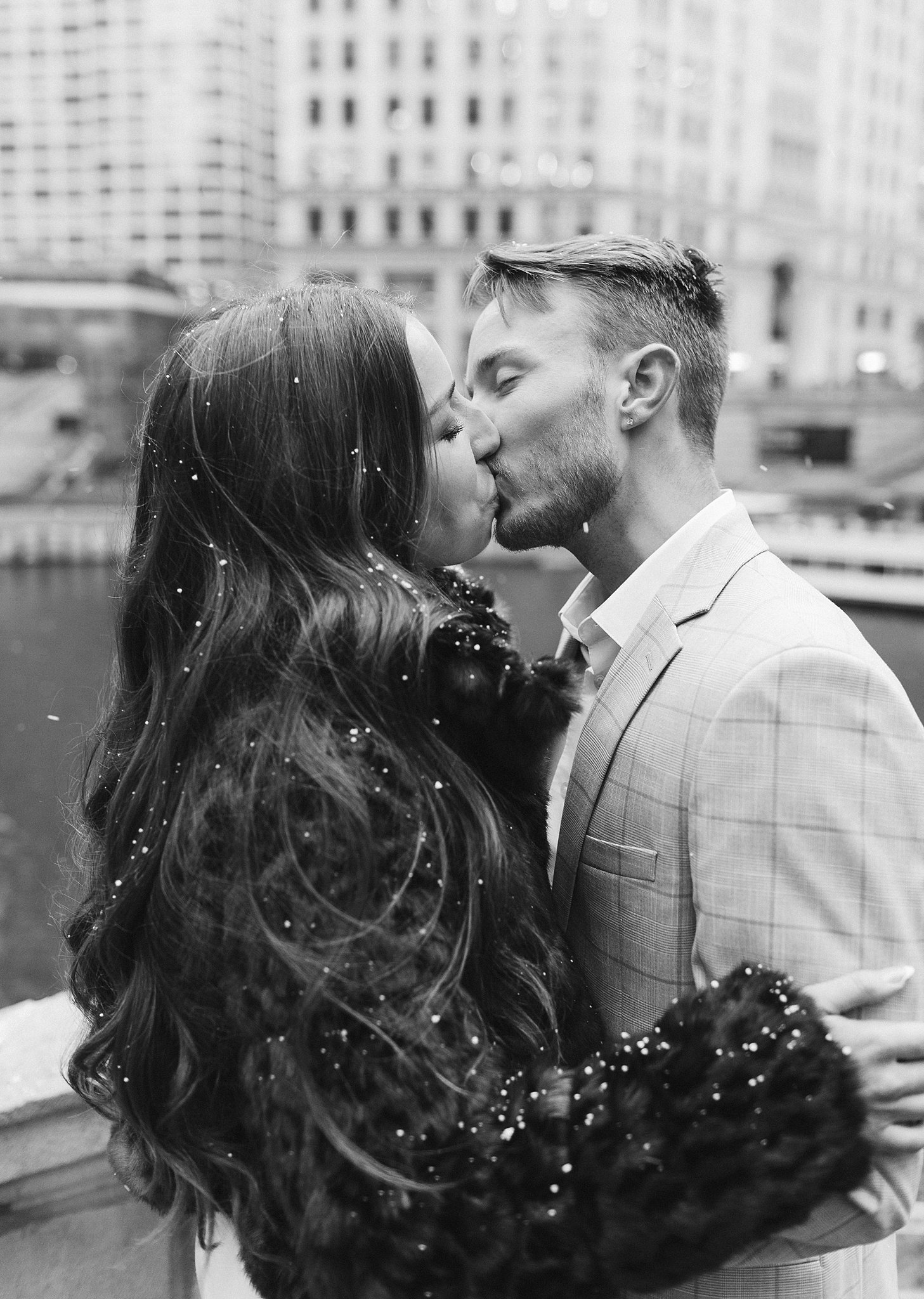 A happy couple kisses on a bridge in the snow during their winter engagement photos in chicago