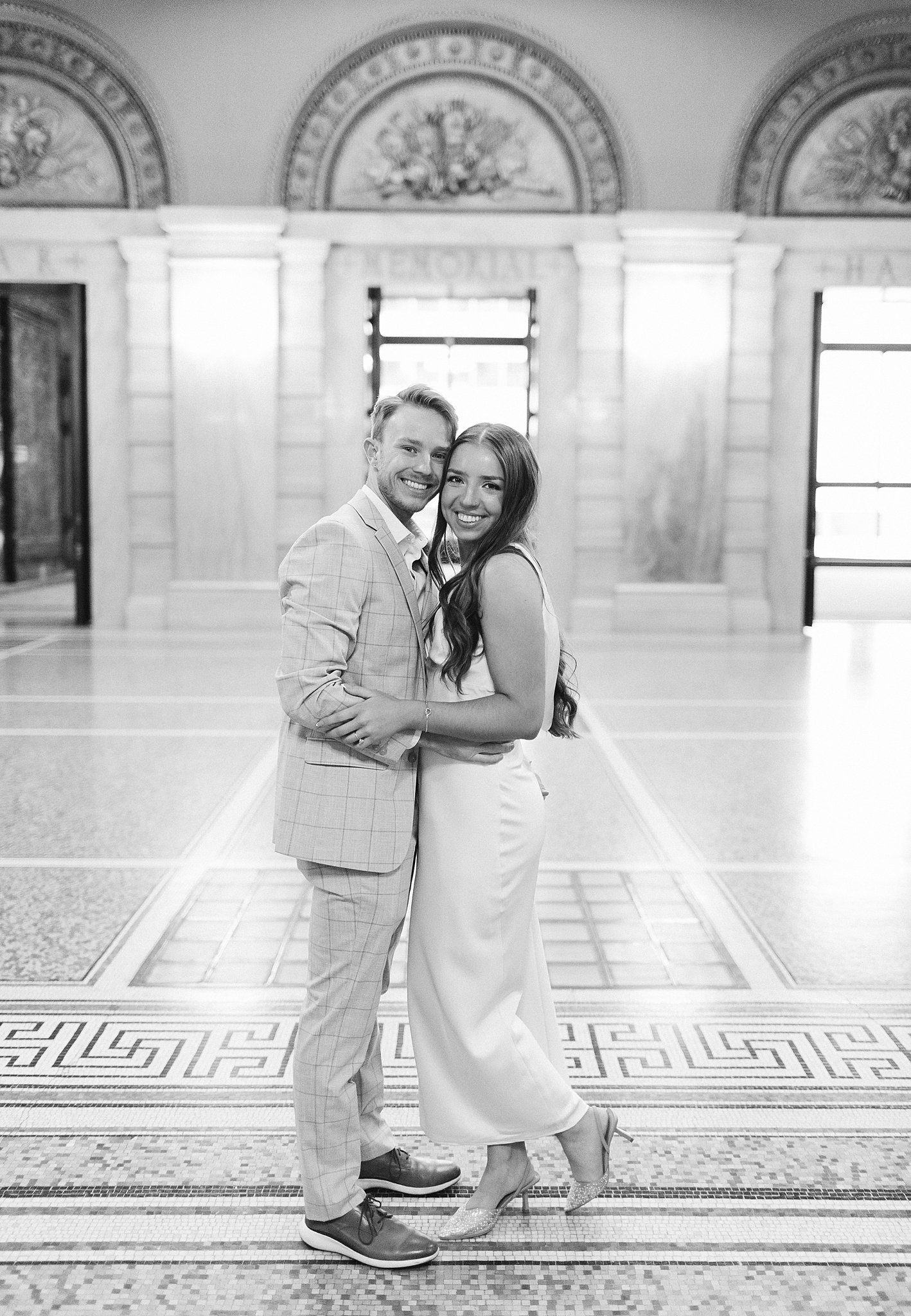 A happy couple touches cheeks in a marble lobby during their winter engagement photos in chicago