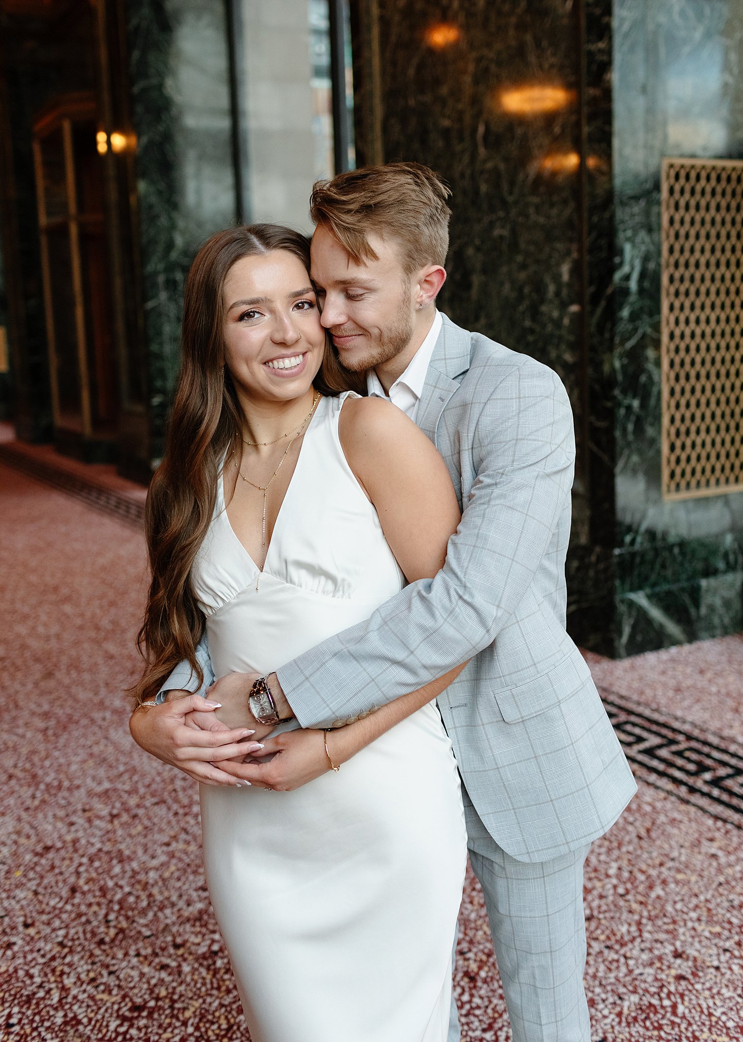 A happy couple snuggles in a marble lobby during their winter engagement photos in chicago