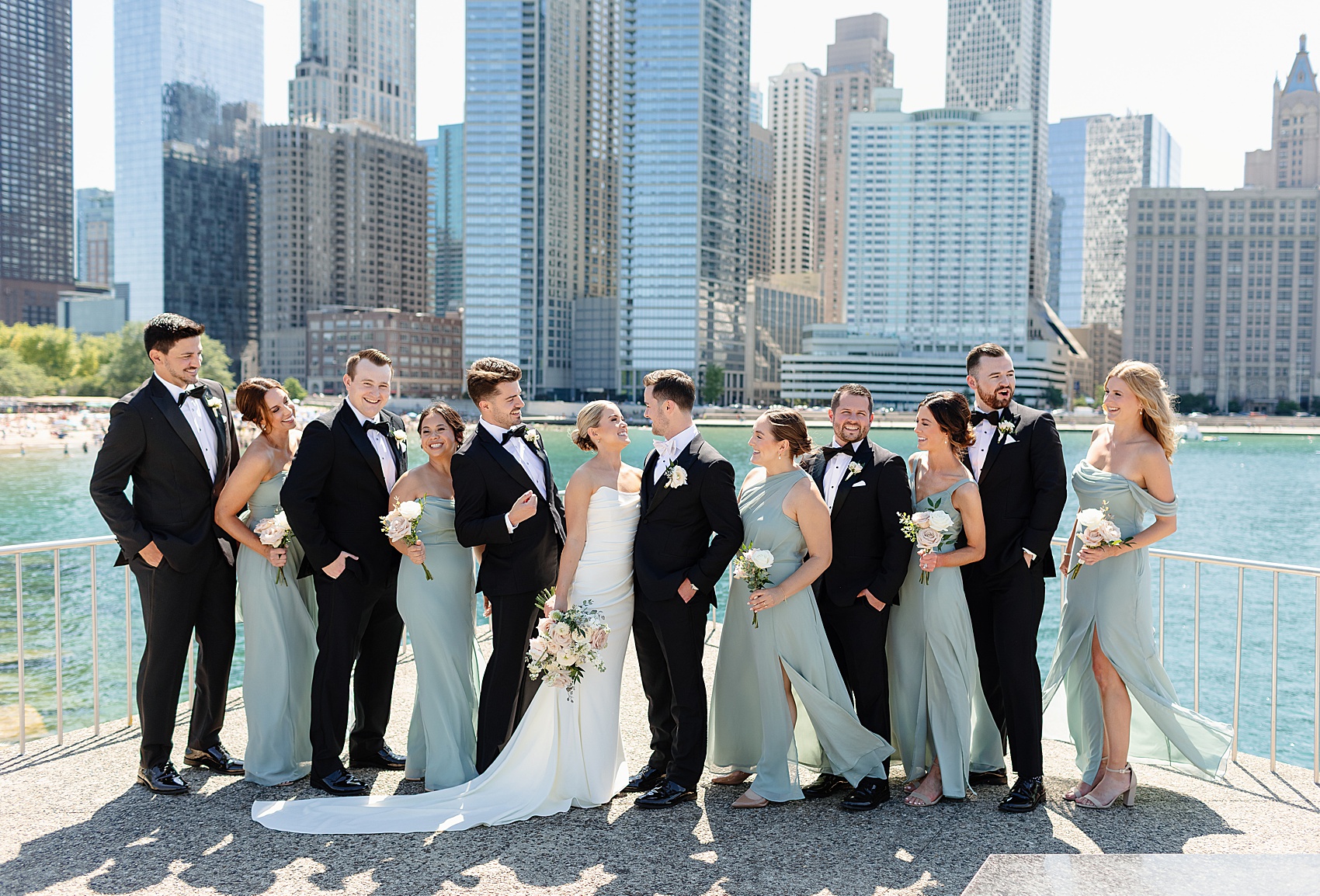 A bride and groom smile at each other while standing with the wedding party on the waterfront at one of the chicago wedding venues with a view
