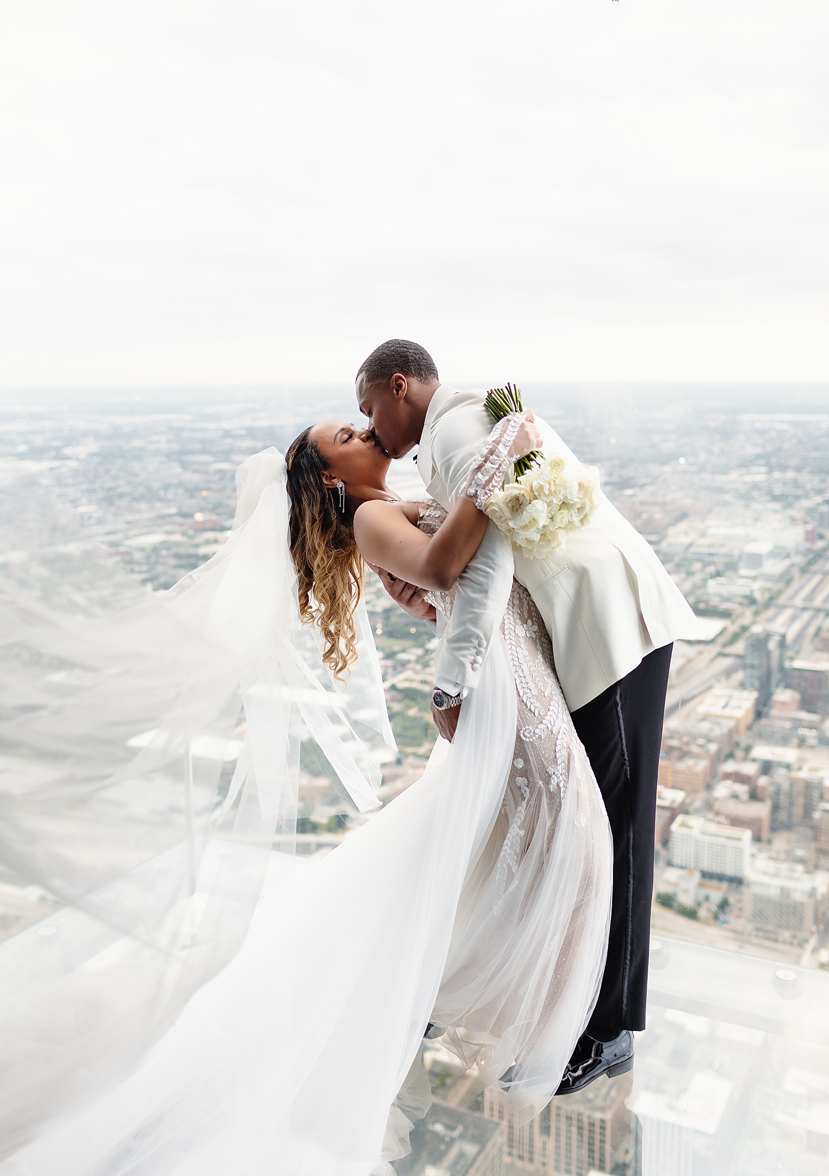 Newlyweds kiss while standing on a glass floor above the city at one of the chicago wedding venues with a view