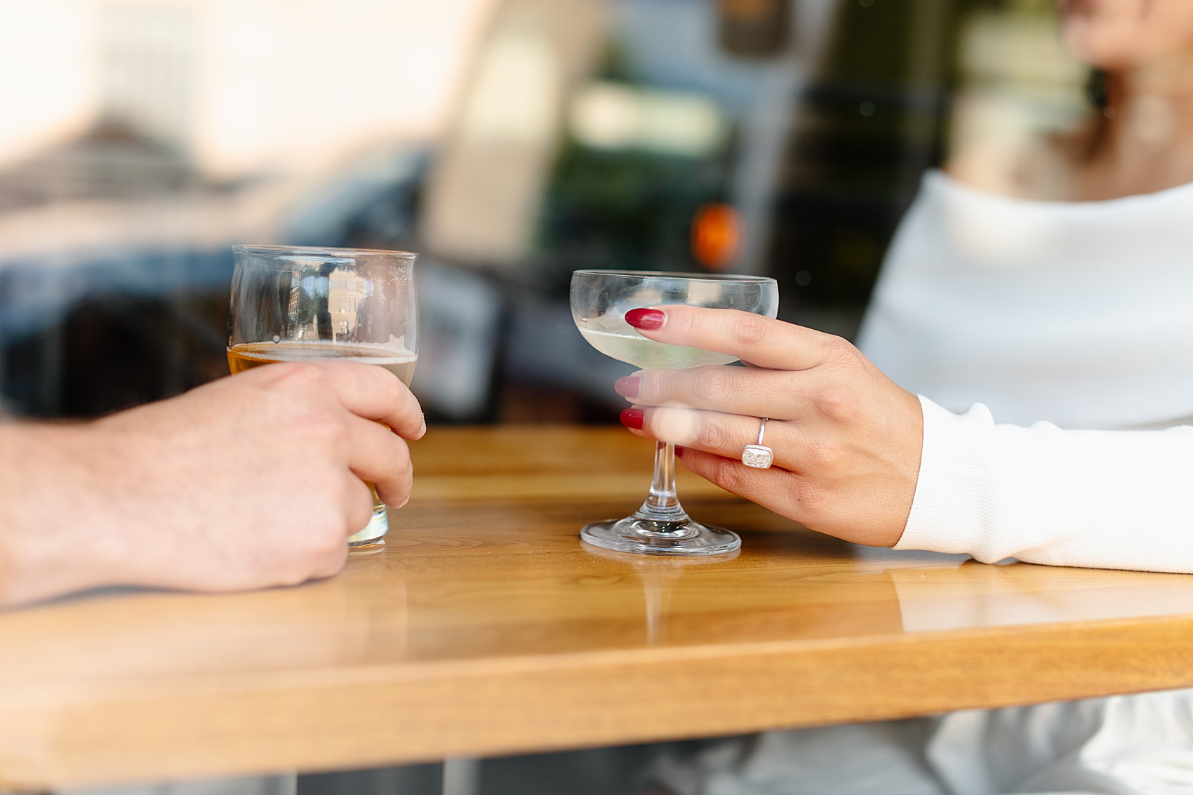 Details of an engaged couple holding cocktails on a table at a bar