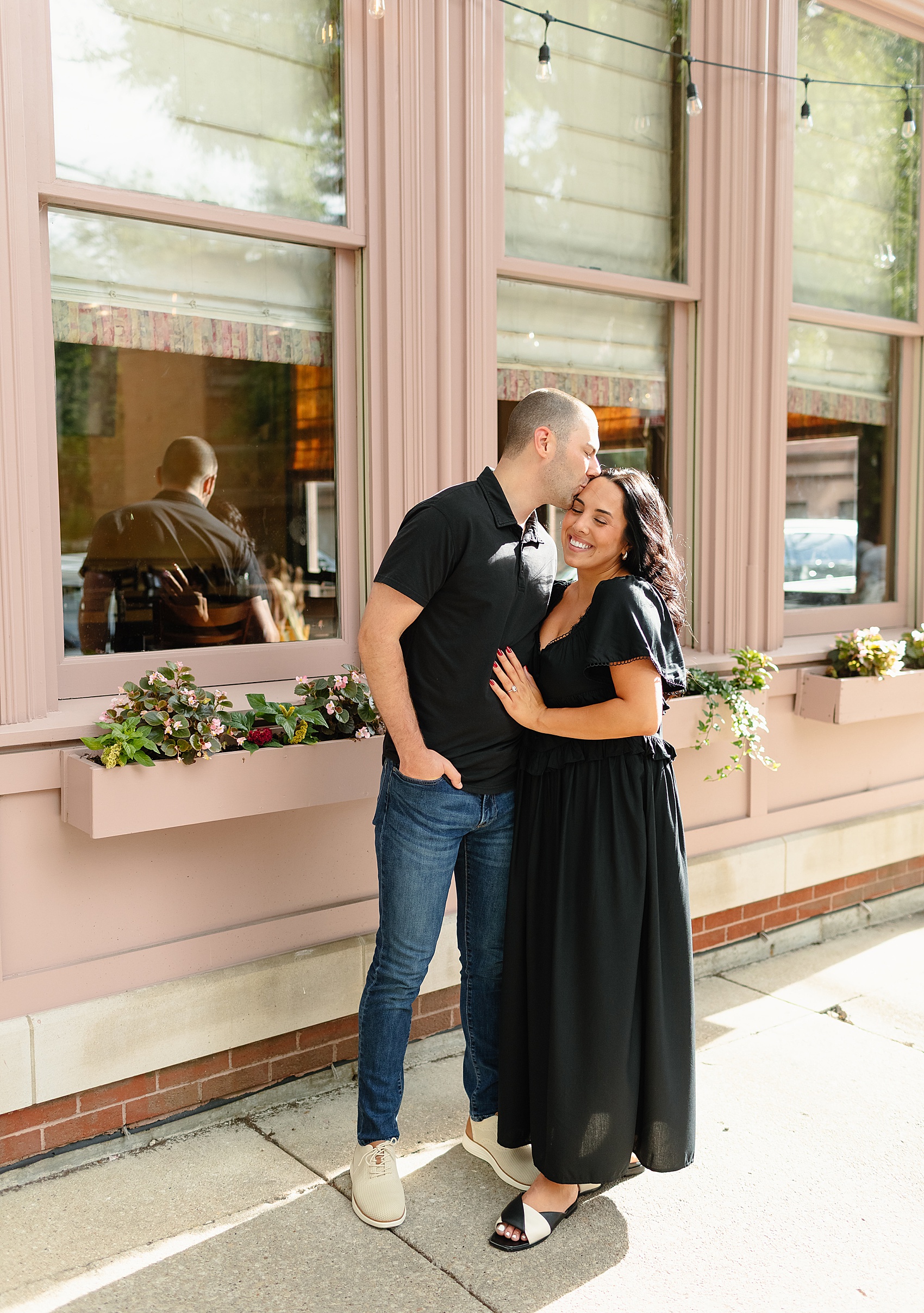 A man in a black polo kisses the head of his fiancee in a black dress while walking downtown with their engagement photo ideas in chicago